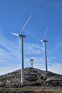 Low angle view of windmills on landscape against sky