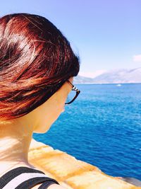 Close-up of woman by blue sea against clear sky on sunny day