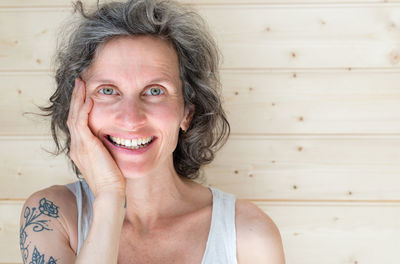 Close-up portrait of happy mature woman with hand on chin by wall