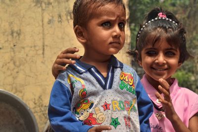 Portrait of smiling sister standing with brother against wall