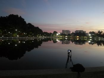 Silhouette of photographing city by lake against sky at sunset