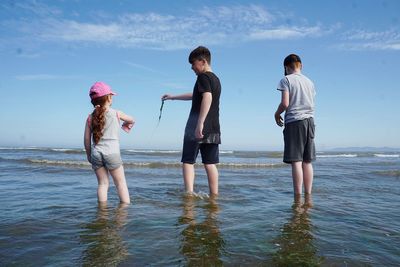 Siblings standing in sea against sky