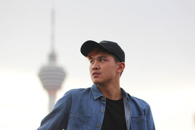 Low angle view of young man looking away while standing against menara kuala lumpur tower