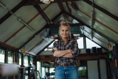 Smiling woman with arms crossed standing at garden shed