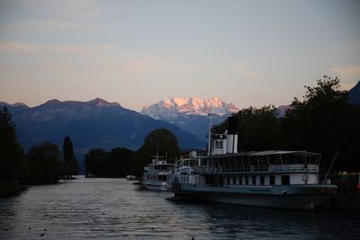 Boats in river against sky during sunset