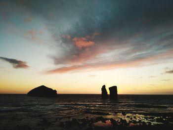 Silhouette rocks on sea against sky during sunset