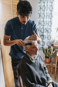 Male care assistant combing hair of senior man at home