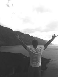 Rear view of man standing on mountain against sky