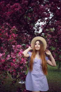 Portrait young beautiful girl teenager in a purple dress and in hat stands blooming pink apple tree