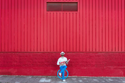 Full length of man riding bicycle standing against red wall