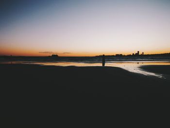 Silhouette person on beach against clear sky during sunset