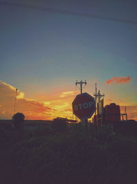 Silhouette cranes on field against sky at sunset