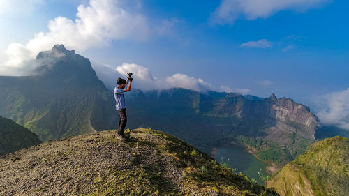 Rear view of man standing on mountain against sky