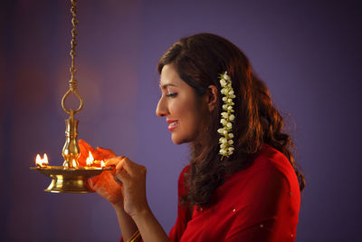 Beautiful indian woman in red sari lighting diya during diwali