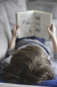 Boy reading book while lying on sofa