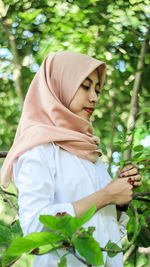 Thoughtful young woman in hijab against tree