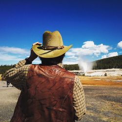 Rear view of cowboy on field against blue sky