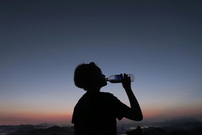 Silhouette of woman standing against sky at sunset