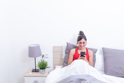 Portrait of young woman using mobile phone while standing against white background