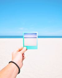 Midsection of person holding blue sea against sky