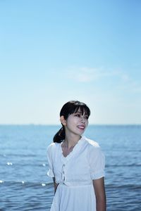 Young woman standing by sea against sky