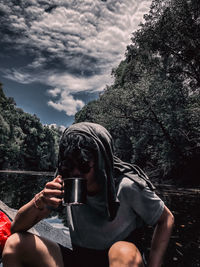 Midsection of man drinking glass on table against trees