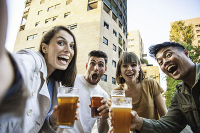 Cheerful friends holding beer while standing outdoors