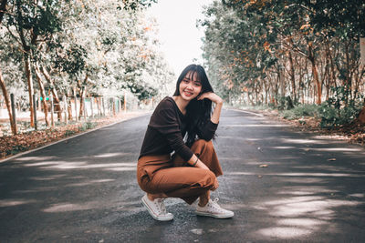 Portrait of young woman sitting on road against trees