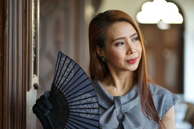 Close-up of woman holding folding fan indoors