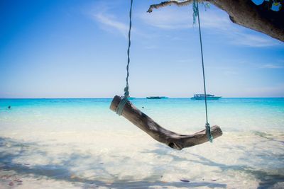 Swing on shore at beach against blue sky