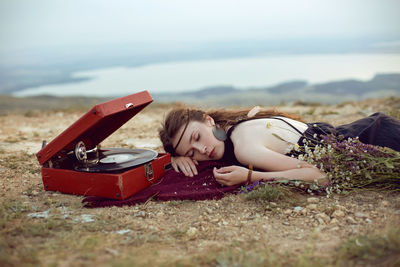 Young woman lies in nature in a black dress next to an old gramophone and listens to music