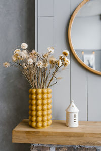 Dried flowers in a yellow ceramic vase in the interior decor of a scandinavian house