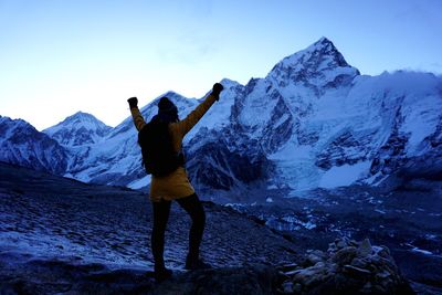Rear view of backpacker with arms raised looking at snowcapped mountains during sunset