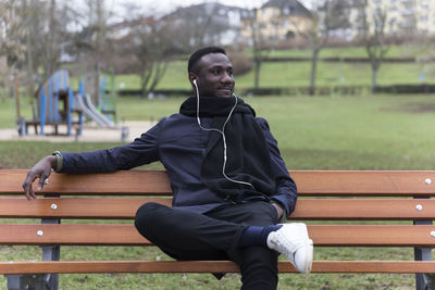 Young man listening music while sitting on bench in park