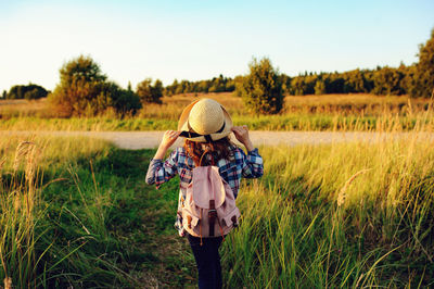 Rear view of girl wearing hat standing on field against sky