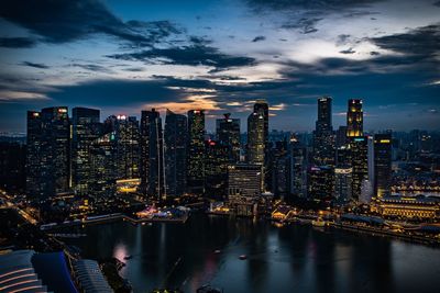 Illuminated buildings by river against sky in city