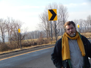 Portrait of mature man smoking while standing on road against sky