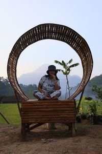 Rear view of man sitting on bench against clear sky