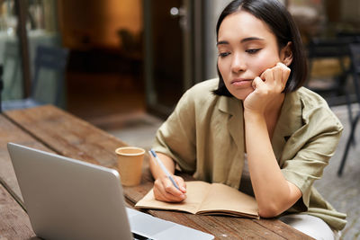 Young woman using laptop while sitting on table