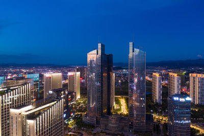 Illuminated buildings in city against clear blue sky