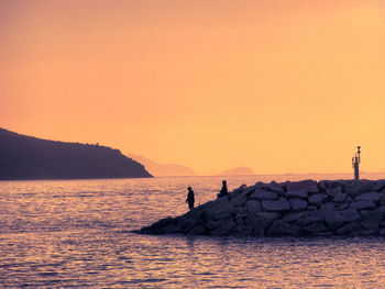 Silhouette people fishing in sea against clear sky during sunset