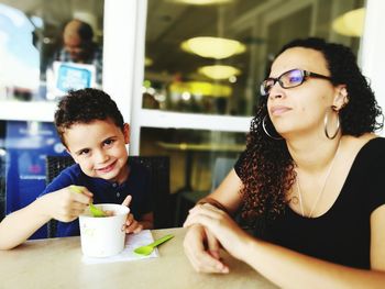 Portrait of cute boy eating food while sitting with mother at table