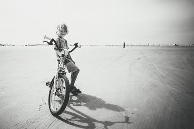 Full length of girl sitting on bicycle at beach against sky