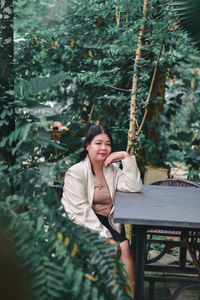 Young woman sitting on plant against trees