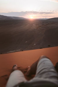 Low section of person relaxing on land against sky during sunset