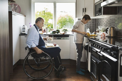 Son with disabled father cutting vegetables in kitchen