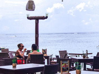 People sitting on table by sea against sky