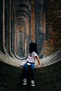 Rear view of woman sitting against brick wall