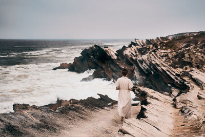 Rear view of man standing on rock by sea against sky