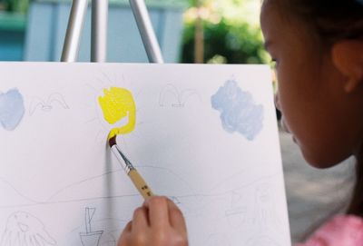 Close-up of girl painting on canvas outdoors